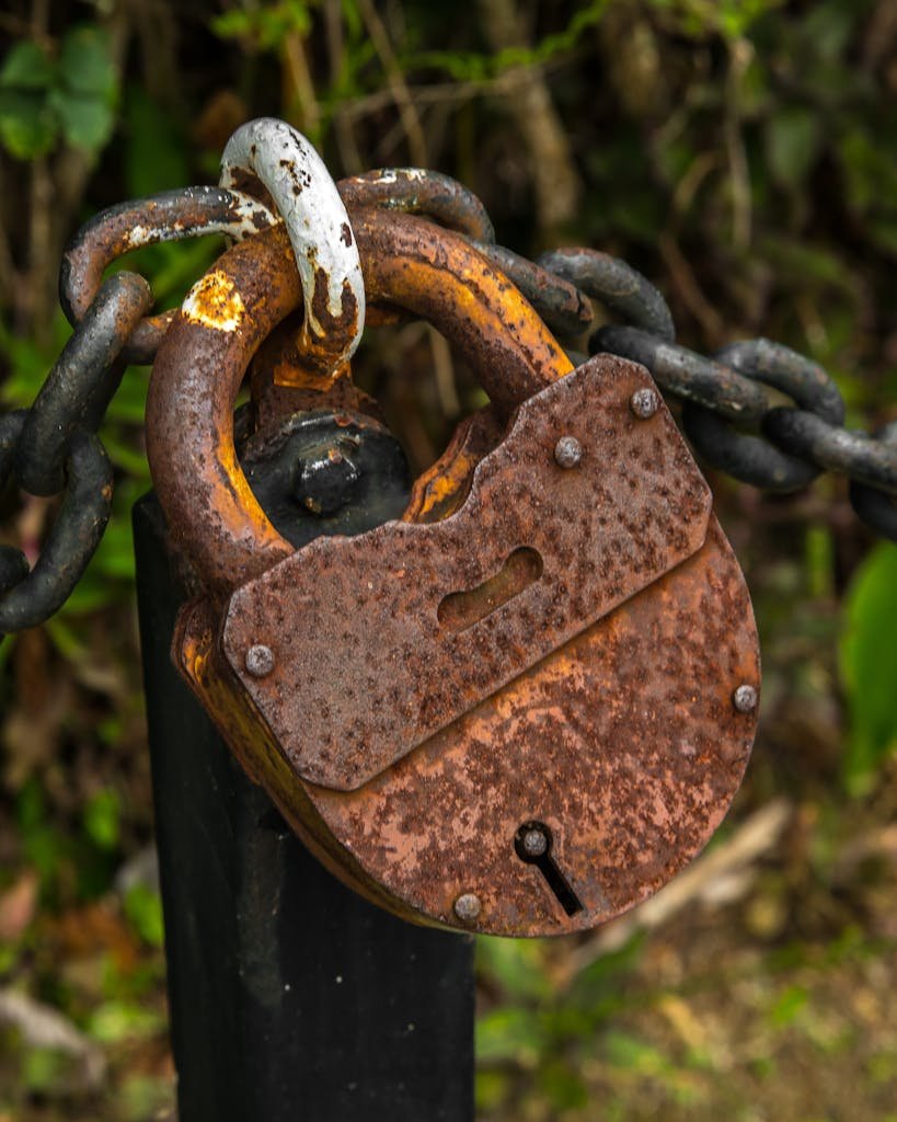 Close-up of a rusty padlock secured to a chain post, symbolizing security.